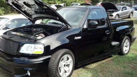 2007 Ford Mustang - Black 2001 Ford F-150 Lightning pickup truck with hood open, parked on grass next to a silver Mustang.