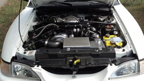 2007 Ford Mustang - The engine bay of a white car is visible, a supercharger and custom intake system.