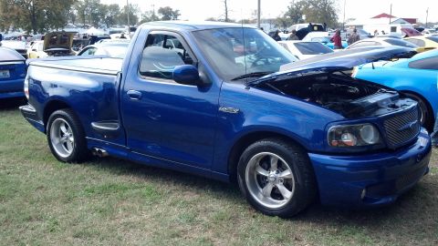 2007 Ford Mustang - A blue Ford F-150 Lightning pickup truck is displayed at an outdoor event with other vehicles around.