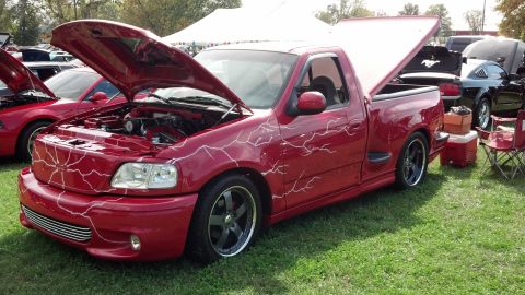 2007 Ford Mustang - A red pickup truck with custom lightning bolt graphics is displayed with its hood and trunk open at an outdoor event.