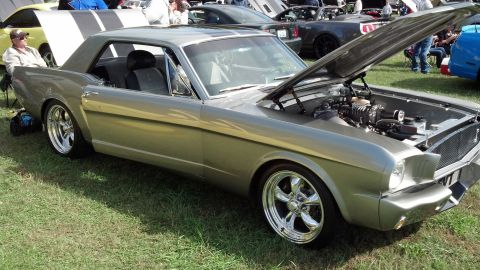 2007 Ford Mustang - A classic Mustang with its hood up, revealing a supercharger, sits on a grassy field among other vehicles.