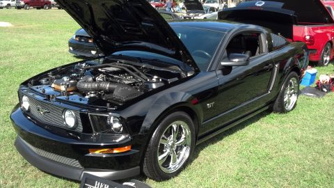 2007 Ford Mustang - A black Ford Mustang GT is displayed with its hood open, alongside other vehicles on a grassy field.