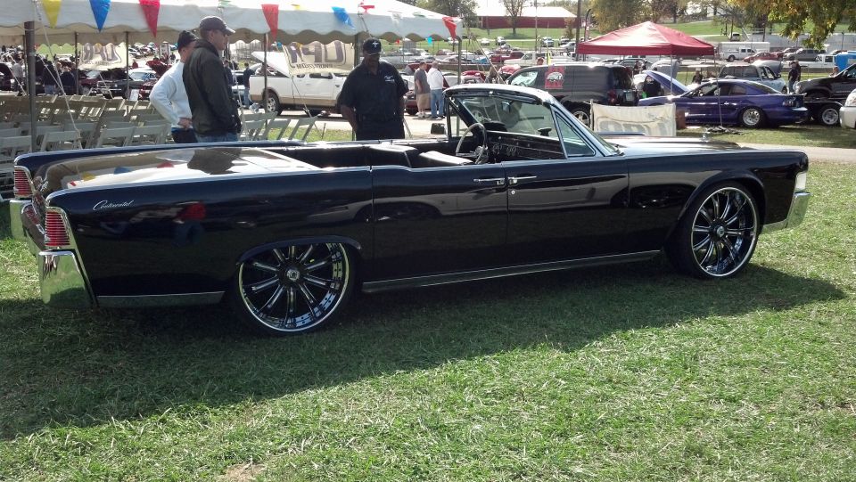Black convertible with chrome trim and large chrome wheels parked on grass