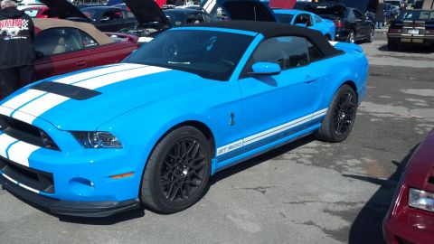 2007 Ford Mustang - A bright blue Ford Mustang convertible with racing stripes is parked at an outdoor car show.