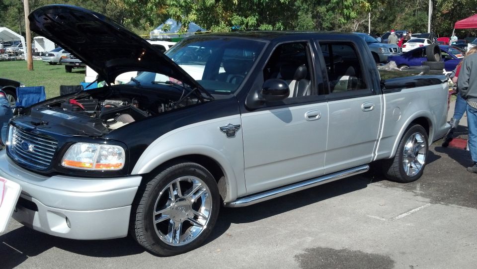 Two-tone silver and black Ford F-150 SVT Lightning pickup truck with hood open, chrome wheels, and side running boards