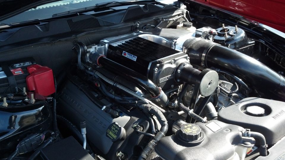 Engine bay with supercharger, battery, and hoses visible. Text on engine reads 'Ford Racing'