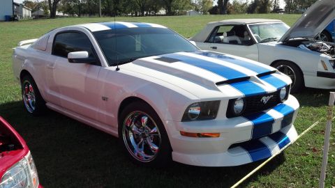 2007 Ford Mustang - A white Ford Mustang GT with blue racing stripes is parked on a grassy field next to other vehicles.