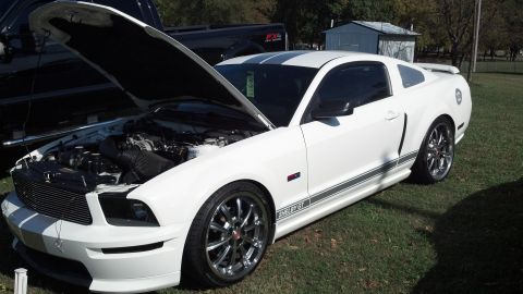 2007 Ford Mustang - A white Ford Mustang Shelby GT is parked on grass with its hood open, revealing the engine compartment.