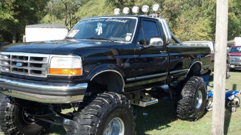 2007 Ford Mustang - A heavily modified black Ford F-350 pickup truck is parked on grass, with a second vehicle visible in the background.