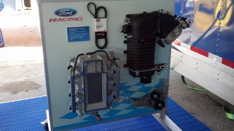 2007 Ford Mustang - A Ford Racing supercharger and belt are displayed on a board, with a blue checkered pattern in the background.