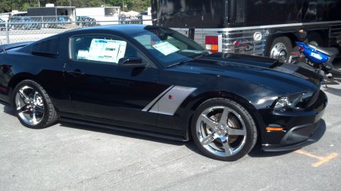 2007 Ford Mustang - A black 2007 Ford Mustang is parked outside, displaying its distinctive side stripe and chrome wheels.