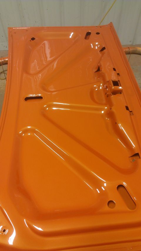 1973 Chevrolet Camaro - The underside of a freshly painted orange car hood is shown, with structural reinforcements visible.