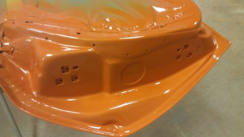 1973 Chevrolet Camaro - The interior of an orange car door shows mounting points and a circular recess, possibly awaiting further assembly or restoration.