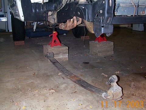 1986 Ford Bronco - Underbody view of a vehicle undergoing suspension work, showing the frame and removed leaf spring.