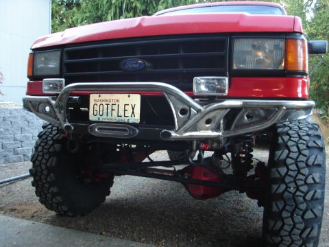 1989 Ford Bronco - Front view of a red Ford truck lifted on large mud-terrain tires, featuring a custom polished tubular steel front bumper and a Washington '…