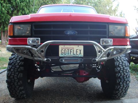 1989 Ford Bronco - Front of a lifted red Ford truck with a custom tube bumper, large mud tires and a Washington 'GOTFLEX' license plate.
