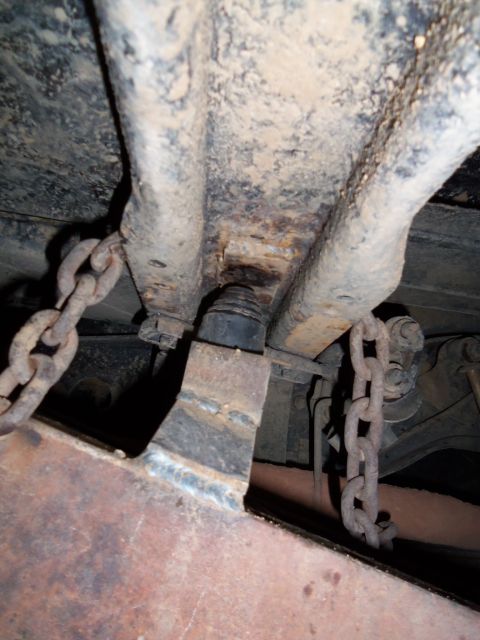 1989 Ford Bronco - Close-up view of the rear suspension system, chains and rusty metal components.