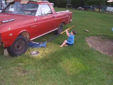 1966 Ford Ranchero - A young boy attempts to jack up a red 1966 Ford Ranchero, which appears to be undergoing some form of maintenance or restoration.
