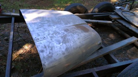 1978 Ford Bronco - A bare metal car hood is on a trailer frame. Tires are visible in the background.