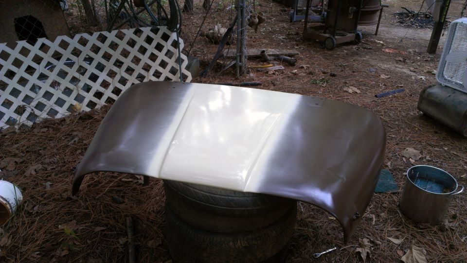 Hood of a vehicle, partially painted white, sitting on tires outdoors