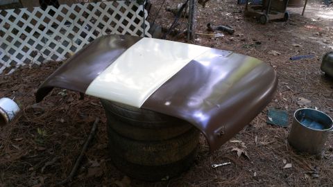 1978 Ford Bronco - Car hood with two-tone paint job sits on stacked tires in a yard.