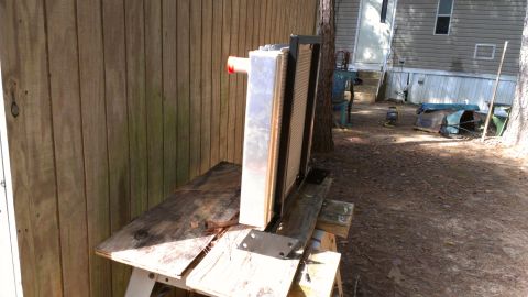 1978 Ford Bronco - A radiator sits on a workbench outside a trailer home, with a wooden fence behind it.