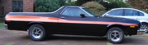 1975 Ford Ranchero - A black 1975 Ford Ranchero with an orange stripe is parked next to a silver sedan.