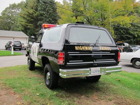 1987 Dodge 1500 - This police SUV, likely from the 1980s, is parked on a grassy area with other vehicles in the background.