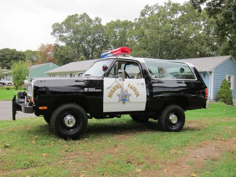 1987 Dodge 1500 - A black and white 1987 Dodge 1500 Ramcharger police SUV is parked on a grassy lawn in front of houses.