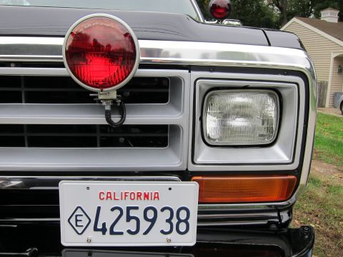 1987 Dodge 1500 - This truck features a prominent red light mounted on its grille, alongside a standard headlight and turn signal.