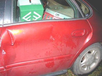 1997 Ford Taurus - The side of a red sedan shows significant damage to the door panel and is loaded with items in the back seat.