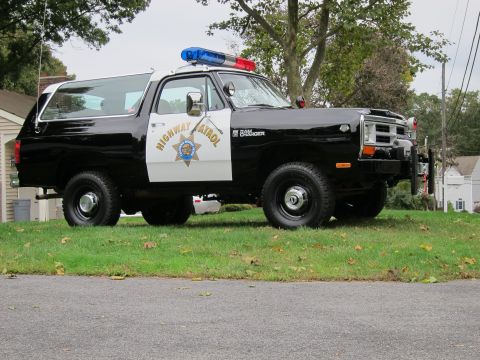 1987 Dodge 1500 - A black and white Dodge Ramcharger police SUV is parked on a grassy lawn, showing its front-right side.