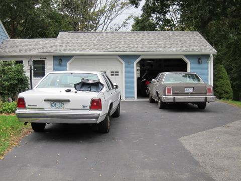 1987 Dodge 1500 - Two sedans are parked in a driveway in front of a blue garage.