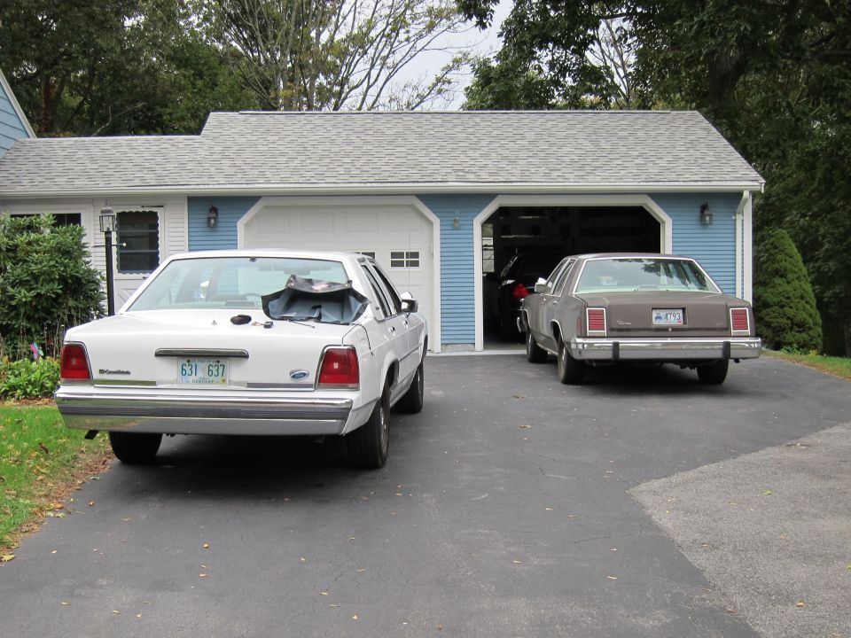 White sedan with a black tarp on its trunk, parked in a driveway