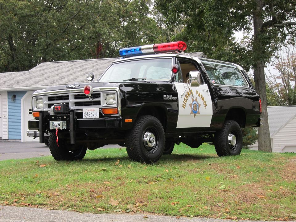 Black and white 1987 Dodge 1500 Ramcharger police SUV with light bar and winch, parked on grass