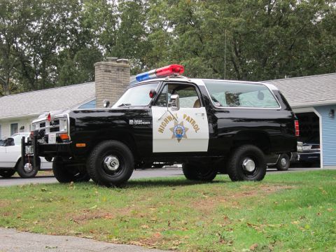 1987 Dodge 1500 - A black and white Dodge Ramcharger police vehicle is parked on a grassy lawn in front of a house.