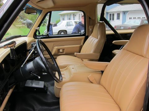 1987 Dodge 1500 - The interior of a truck shows tan bucket seats and a view of houses and a man outside the vehicle.