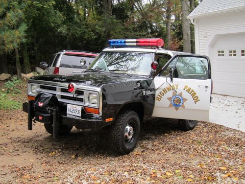 1987 Dodge 1500 - A Dodge Ram pickup truck, modified as a highway patrol vehicle, is parked in front of a garage.