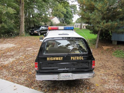 1987 Dodge 1500 - Rear view of a black highway patrol SUV with a light bar and "HIGHWAY PATROL" text on the tailgate.