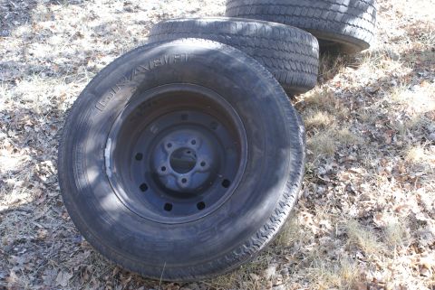 1978 Ford Bronco - A stack of three tires rests on dry leaves and grass, with the closest tire showing its tread pattern and rim.