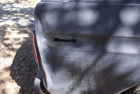 1978 Ford Bronco - Close-up of a dented rear quarter panel on a dark vehicle, with a red taillight on the left.
