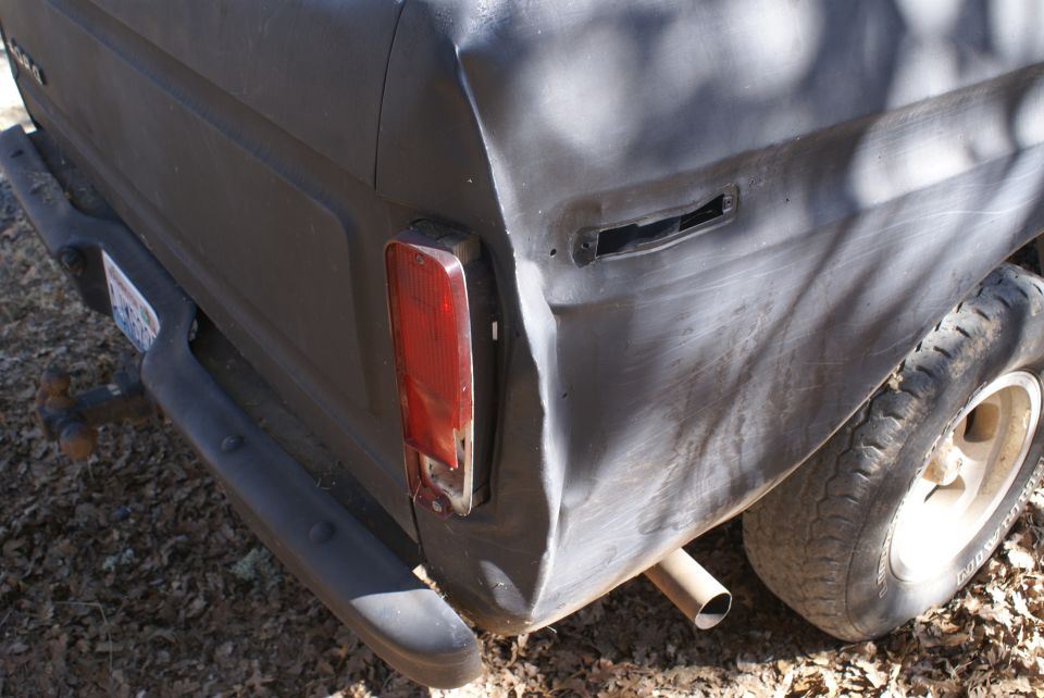 Rear corner of a dark-colored pickup truck, showing a taillight, bumper, and tire