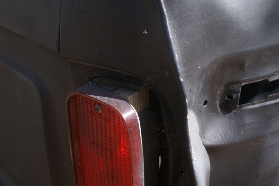 Dark colored vehicle rear corner with a red taillight assembly and visible mounting holes