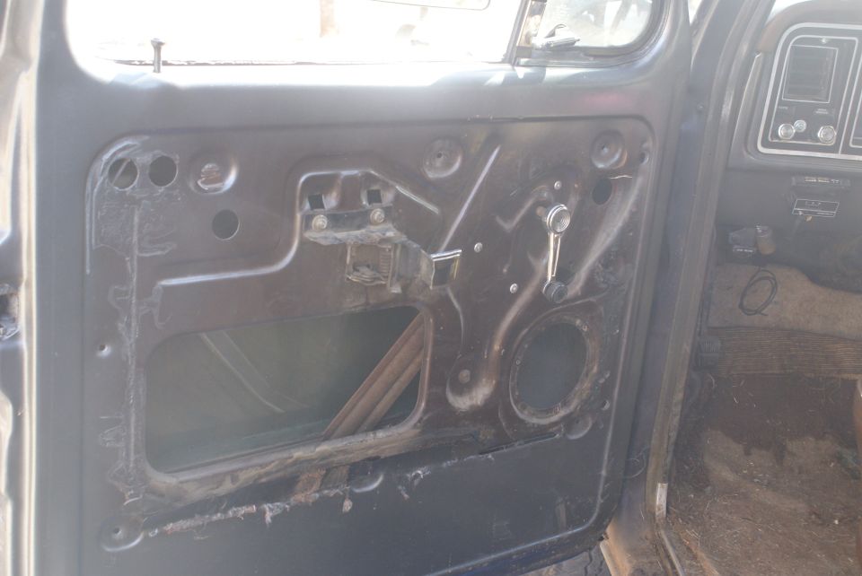 Interior of a vehicle door, showing exposed metal and window mechanism. Dashboard visible to the right