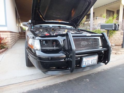 2003 Ford Crown Victoria - Black sedan front with grille guard and hood up, California plate reads EVIL VIC.