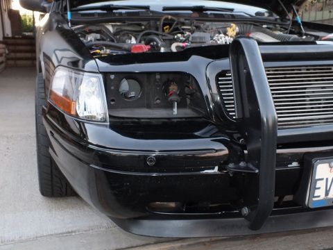 2003 Ford Crown Victoria - Close view of a black sedan front corner with the headlight pulled to expose wiring.