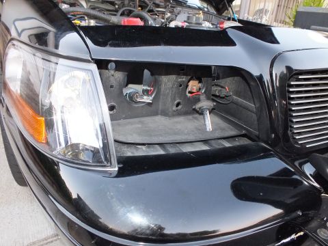 2003 Ford Crown Victoria - Vacant headlight housing on a black car reveals bulb socket and harness plugs.