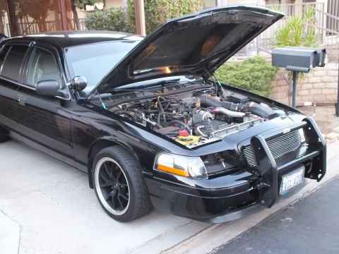2003 Ford Crown Victoria - Front three-quarter of a black sedan, hood up showing engine, parked by a house.