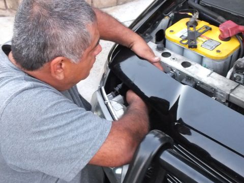 2003 Ford Crown Victoria - Person works on a black car front panel with engine bay and battery exposed.