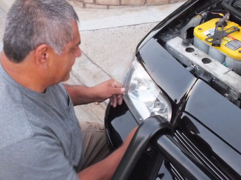 2003 Ford Crown Victoria - Person test-fits a reflector headlight onto a black car with brush guard below.
